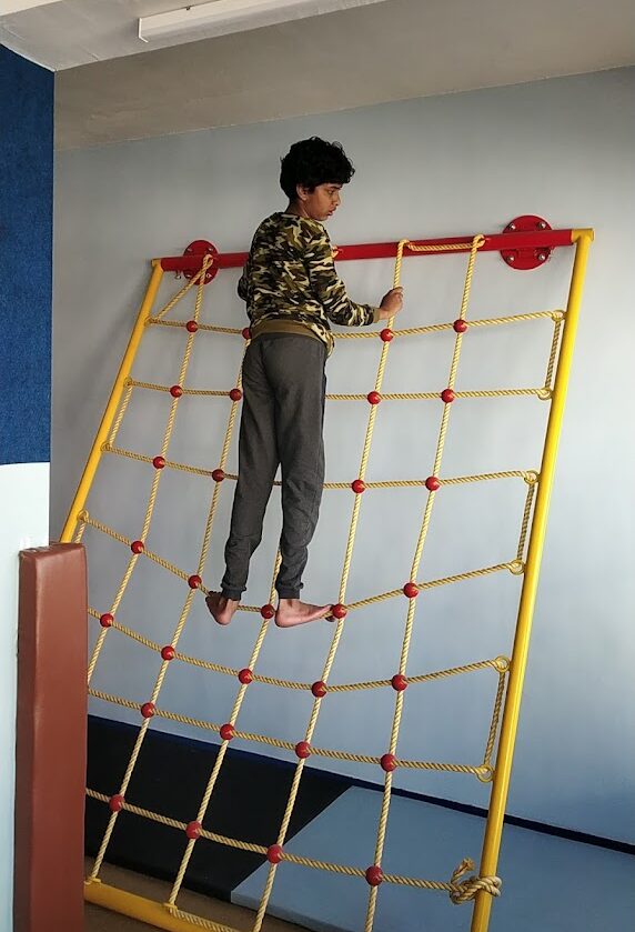 Focused child climbing a rope ladder in an indoor play gym, encouraging physical fitness and confidence.