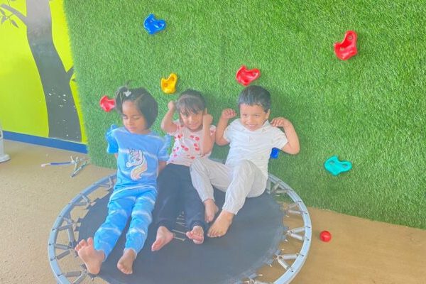 Happy kids resting after gymnastics class on a trampoline in Ahmedabad, with a playful green wall adding to the fun atmosphere.