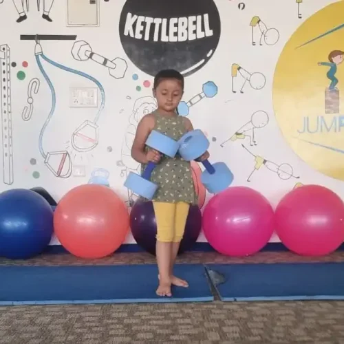 A young child at Jump-n-Rise gym, standing with exercise equipment, illustrating a blog post about the impact of gym activities on height growth in children.