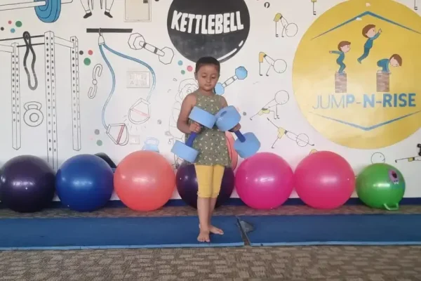 A young child at Jump-n-Rise gym, standing with exercise equipment, illustrating a blog post about the impact of gym activities on height growth in children.