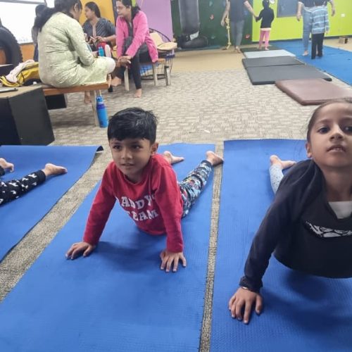 Kids practicing yoga on blue mats in a spacious indoor play gym, promoting health and balance.