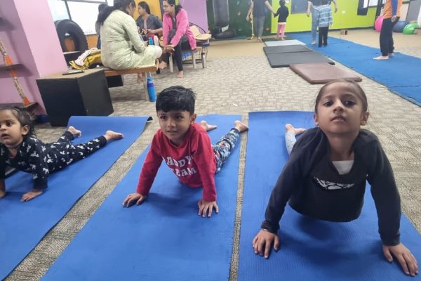 Kids practicing yoga on blue mats in a spacious indoor play gym, promoting health and balance.